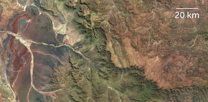 An aerial view of a landscape, with a brown plateau on the right side and greener lowlands on the left side.